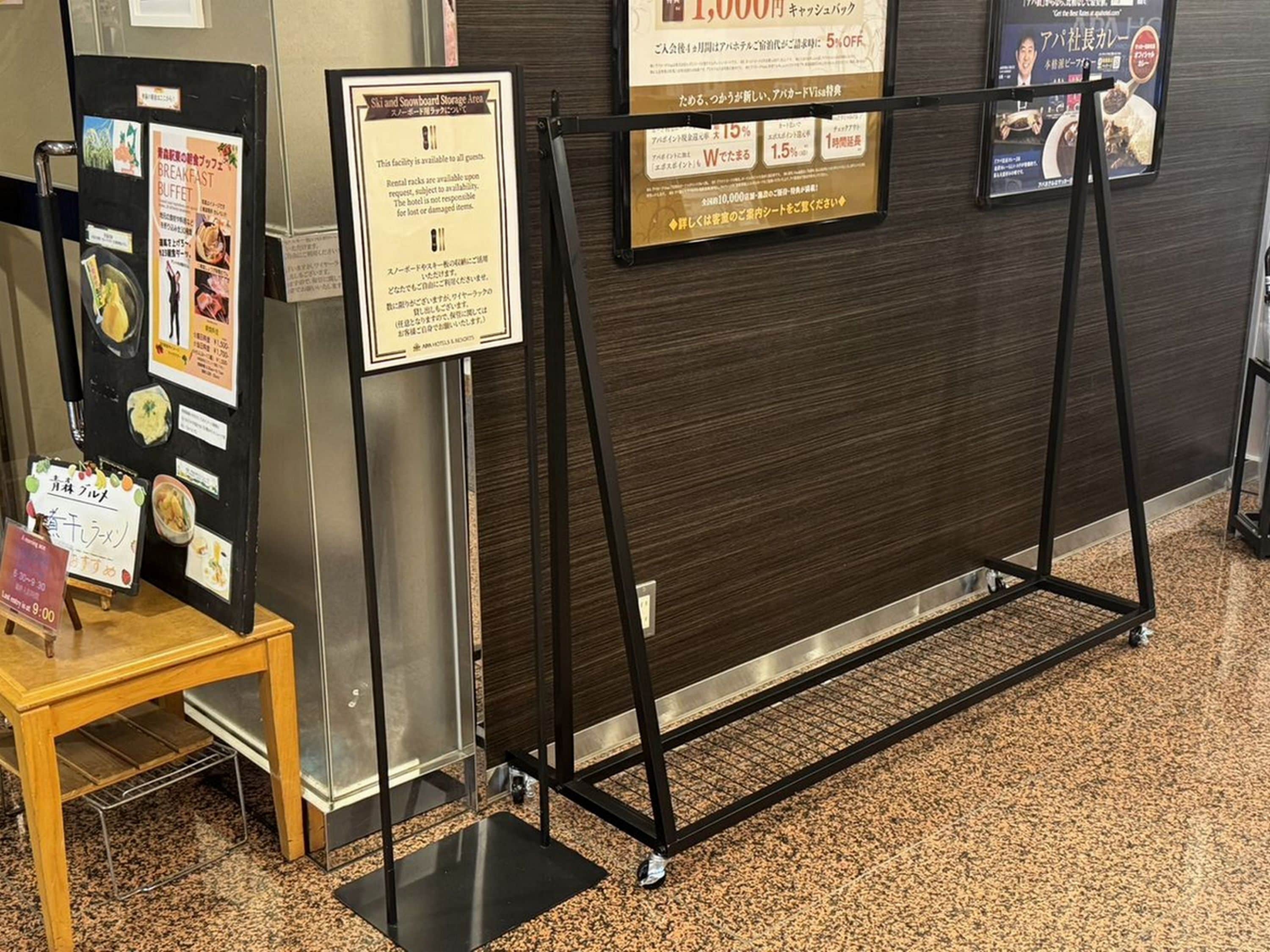 A hotel reception area with a wooden table displaying breakfast options, a sign about ski and snowboard storage, and a promotional poster.
