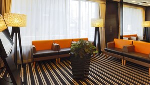 Een hotelhal met een gestreept tapijt, oranje banken en vloerlampen.