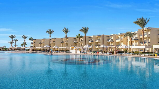 Un complex turístic amb piscina, palmeres i un cel blau radiant.