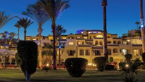 Un hotel amb diverses terrasses, palmeres i una façana ben il·luminada.