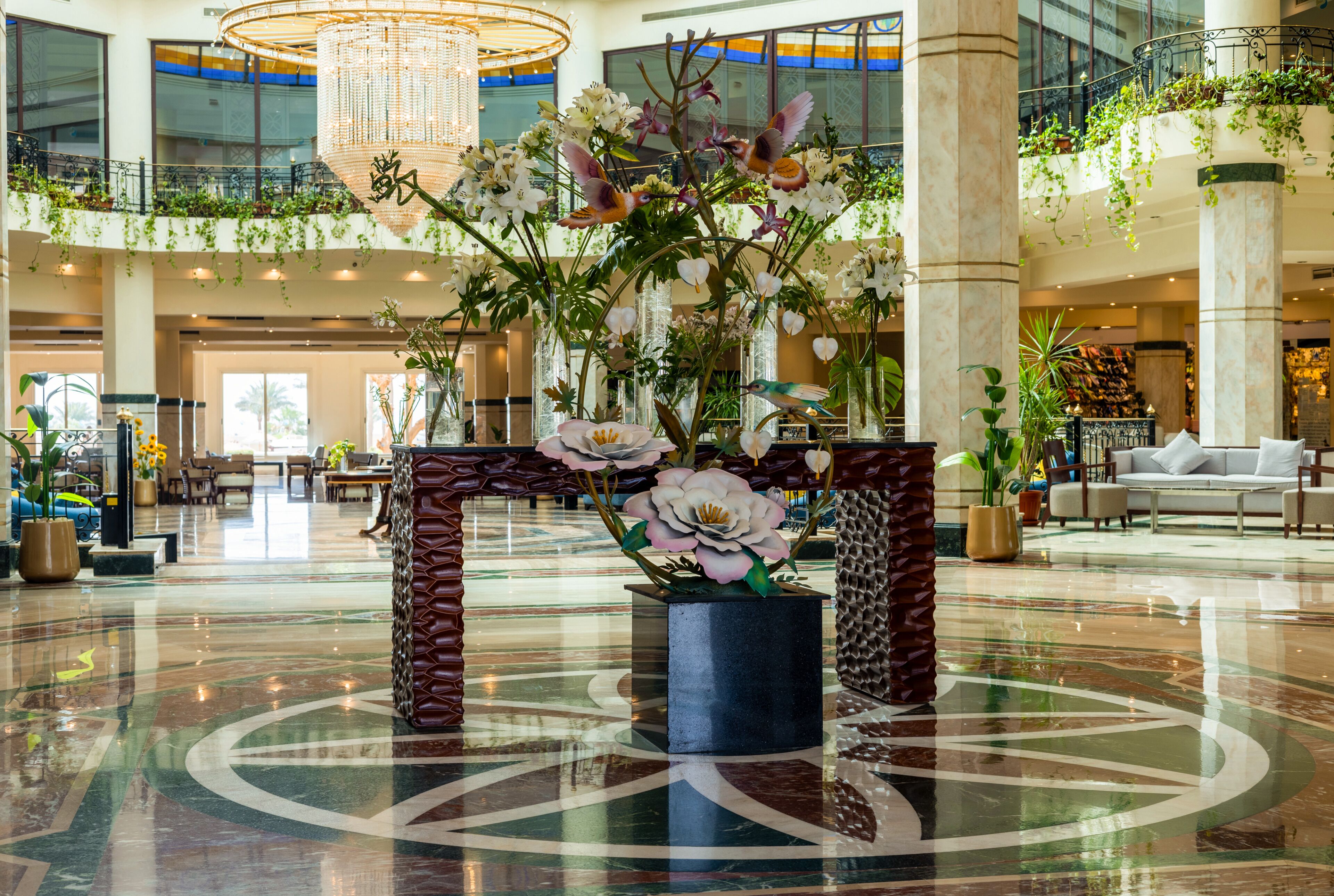 Un hall d’entrée spacieux agrémenté d’une composition florale centrale, doté de hauts plafonds et d’un lustre moderne.
