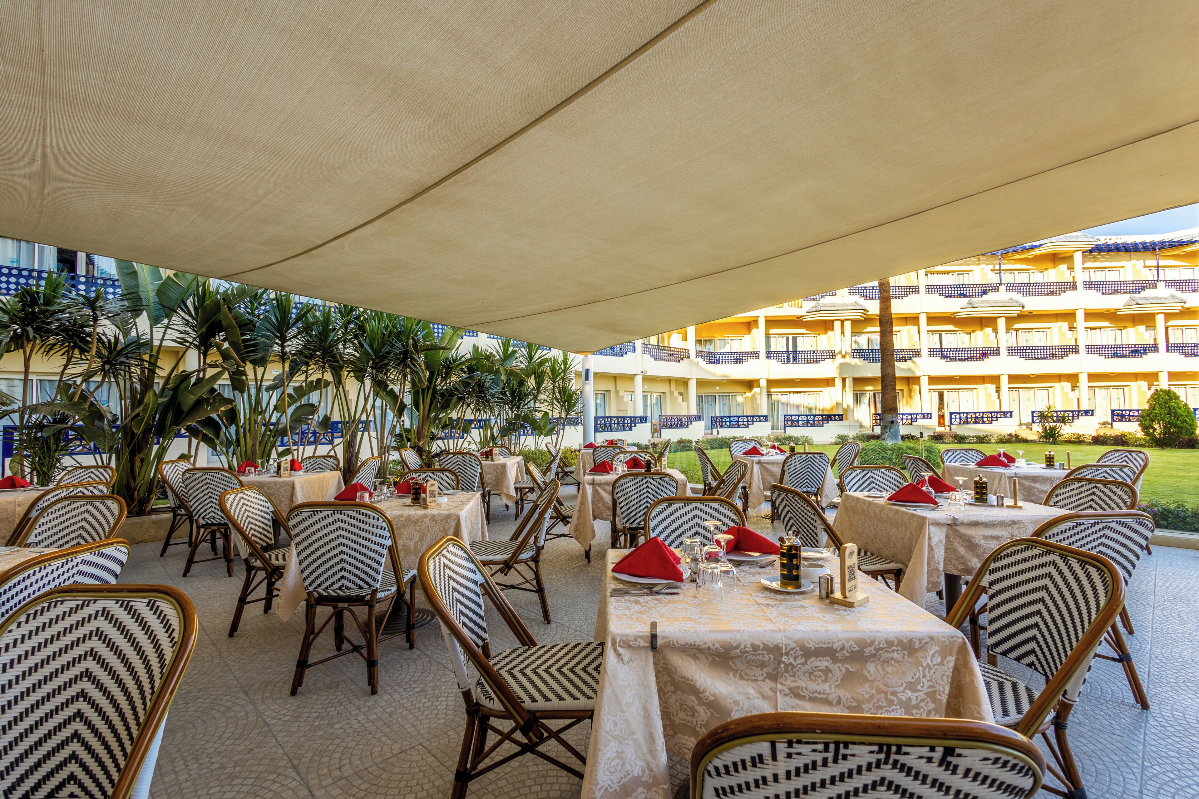 An outdoor dining area with tables and chairs, a covered section, and a building with balconies in the background.