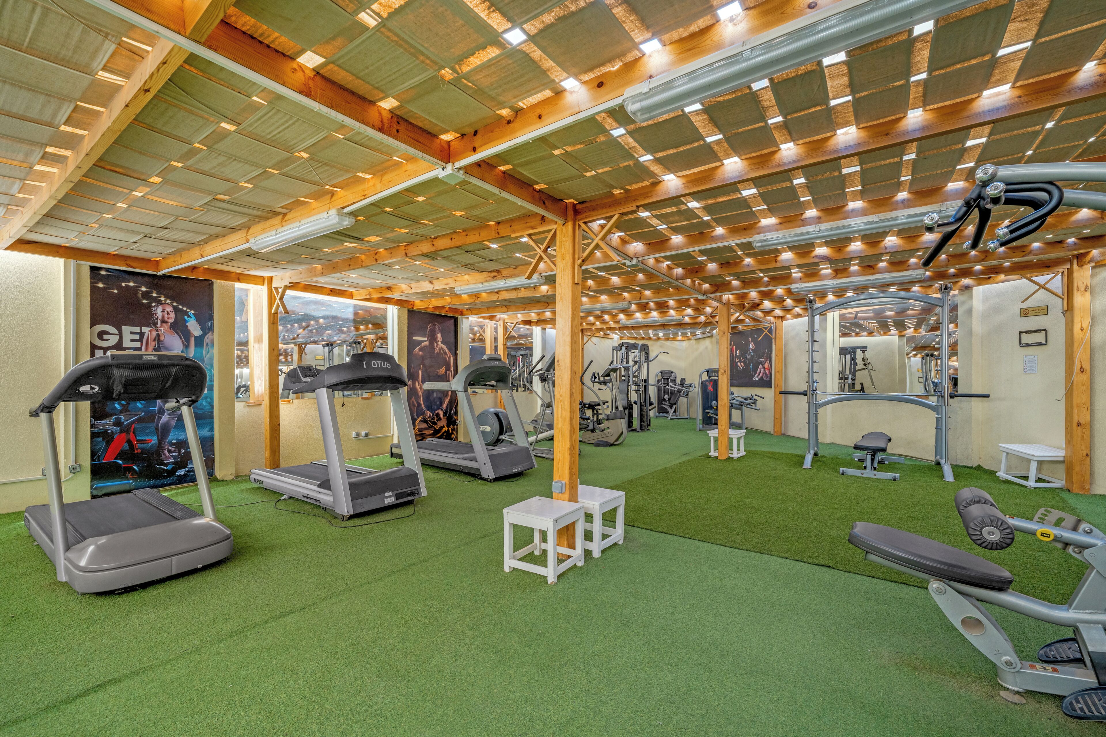 Un gimnasio con cintas de correr, máquinas de pesas y un suelo de césped artificial verde.