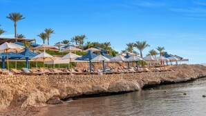 Un hotel de platja amb gandules i paraigudes, una paret de pedra i palmeres.