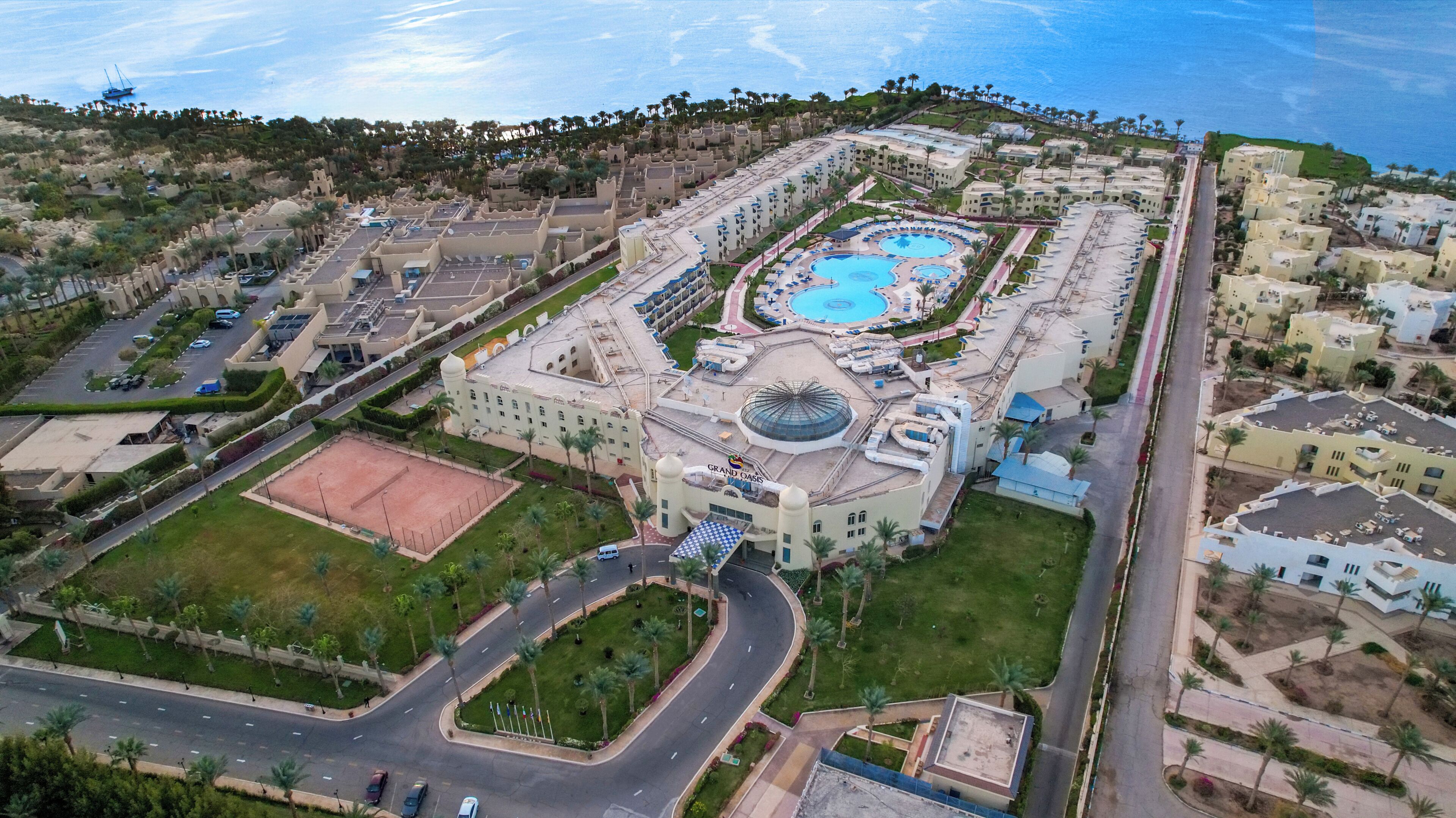 Vue aérienne d’un hôtel doté d’une grande piscine centrale, de plusieurs bâtiments et d’un espace paysager environnant.
