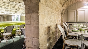A restaurant with wicker chairs, a green booth, and a stone wall. - Hôtel Jardin le Bréa (Paris)
