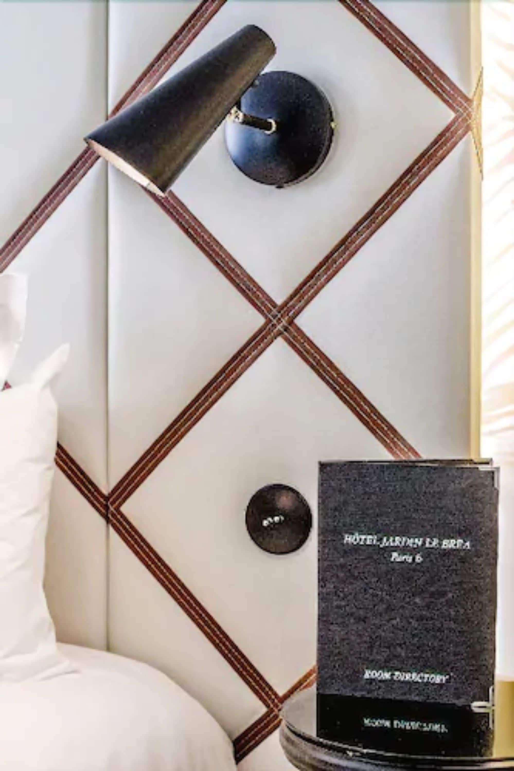 Une pièce avec un lit blanc, une lampe noire et un panneau noir portant une inscription.