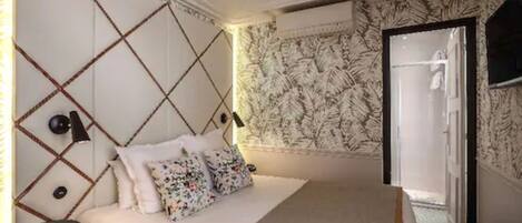 Habitación de hotel con cama, mesita de noche, lámpara y papel tapiz estampado.