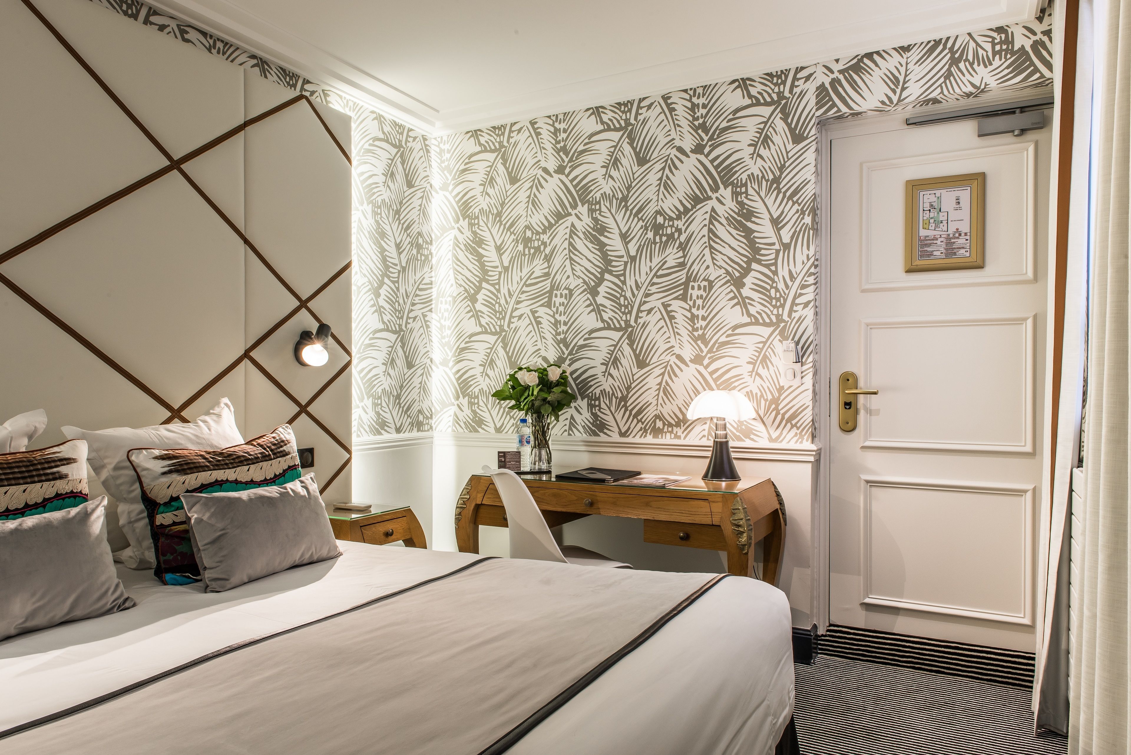 A hotel room with a bed, a desk, and a door.