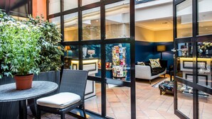 A cozy indoor seating area with a round table and chairs, a potted plant, and a bookshelf filled with books and magazines. - Hôtel Jardin le Bréa (Paris)