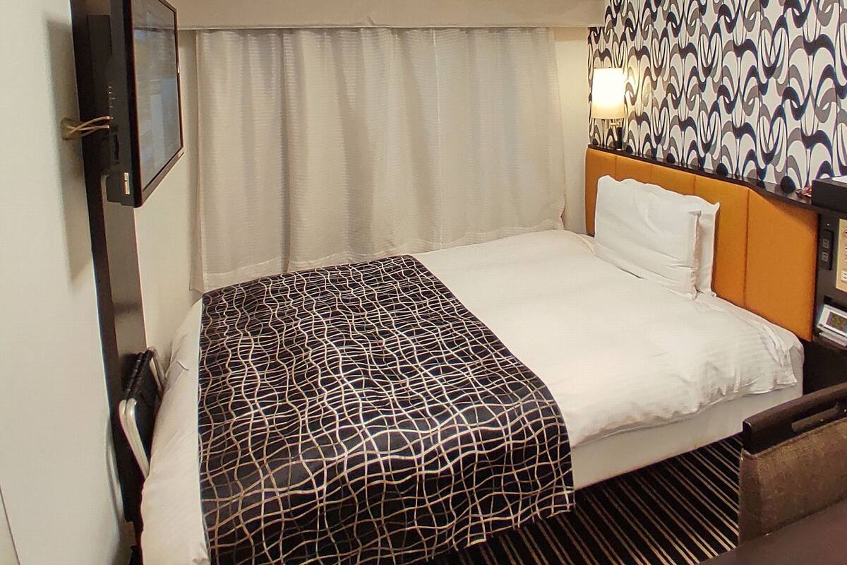 A hotel room with a bed, a bedside table, a lamp, and a patterned wall.