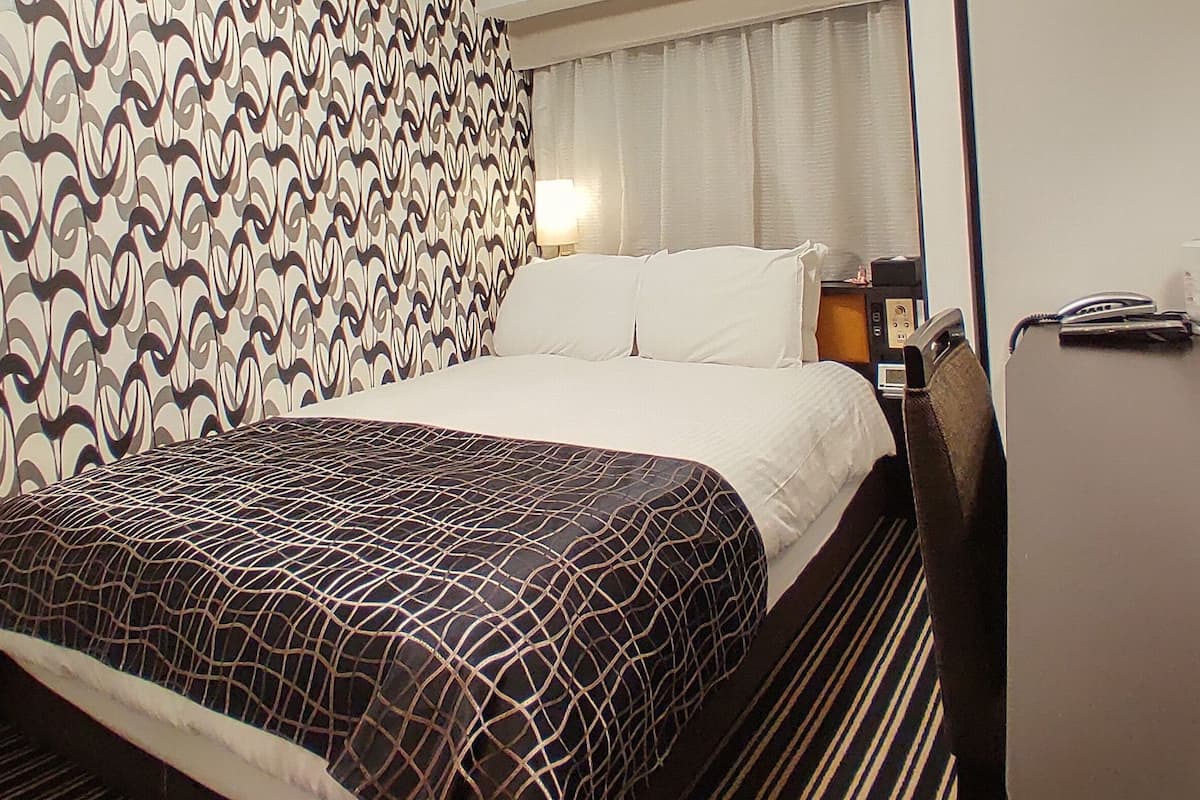 A hotel room with a bed, a desk, a telephone, and a lamp.