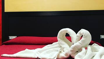 A bed with red bedding and two white towels arranged in a heart shape.