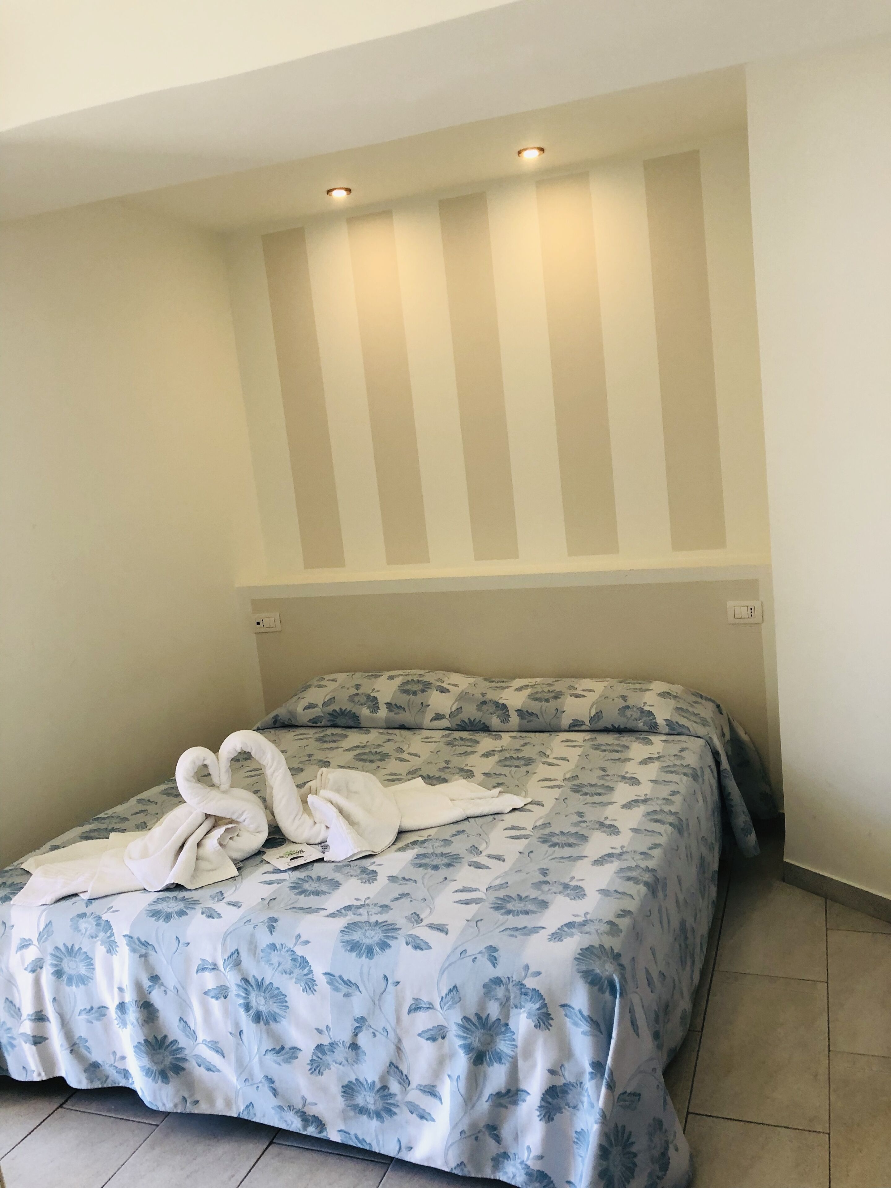 Habitació d'hotel amb un llit, una colcha amb motius florals i tovalloles amb forma de cigne.