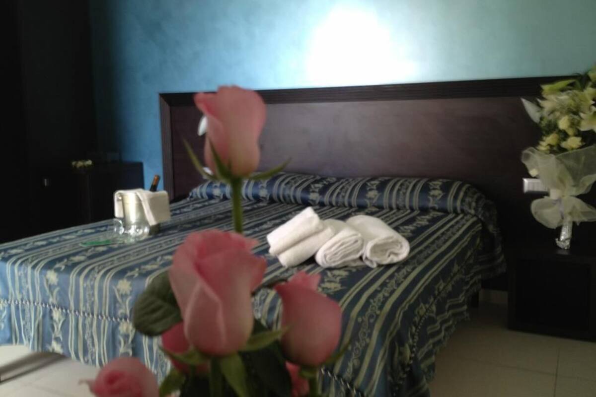 Une chambre avec une couvre-lit à motifs bleus et blancs, une tête de lit en bois et un bouquet de roses roses sur le lit.