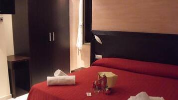 A hotel room with a large bed, dark wooden wardrobe, and a flat-screen TV mounted on the wall.