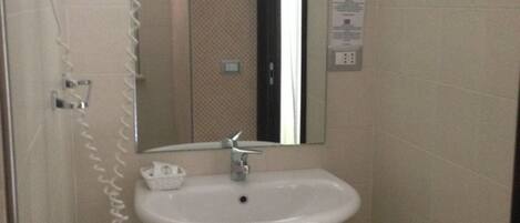 A bathroom with a white sink, a mirror, a hairdryer, and a trash bin.