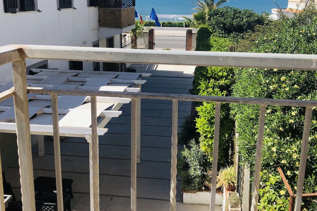 Un balcon avec vue sur la mer, un bâtiment blanc et quelques plantes.