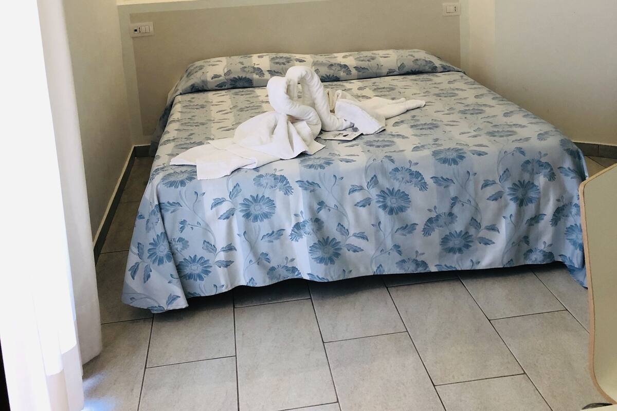 Une chambre d’hôtel avec un lit, une couvre-lit à motifs floraux et une disposition artistique des serviettes.