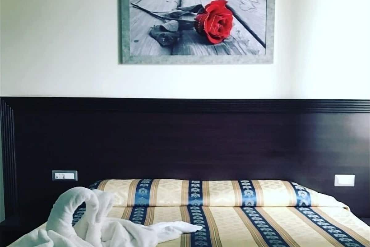 Un lit avec une couvre-lit à rayures, un tableau encadré représentant une rose accroché au mur et une serviette blanche posée sur le lit.