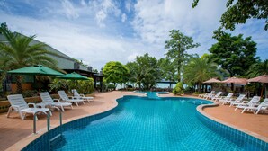 A swimming pool with white lounge chairs and green umbrellas, surrounded by trees and a building with a tiled roof. - Phi Phi Andaman Beach Resort (Ko Phi Phi)