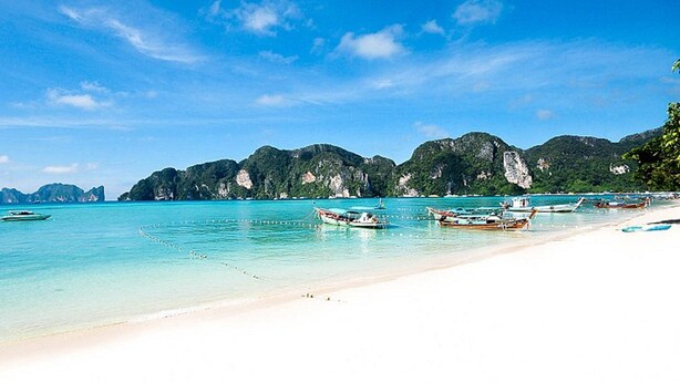 A beach with clear turquoise water, boats, and rocky cliffs in the background. - Phi Phi Andaman Beach Resort (Ko Phi Phi)