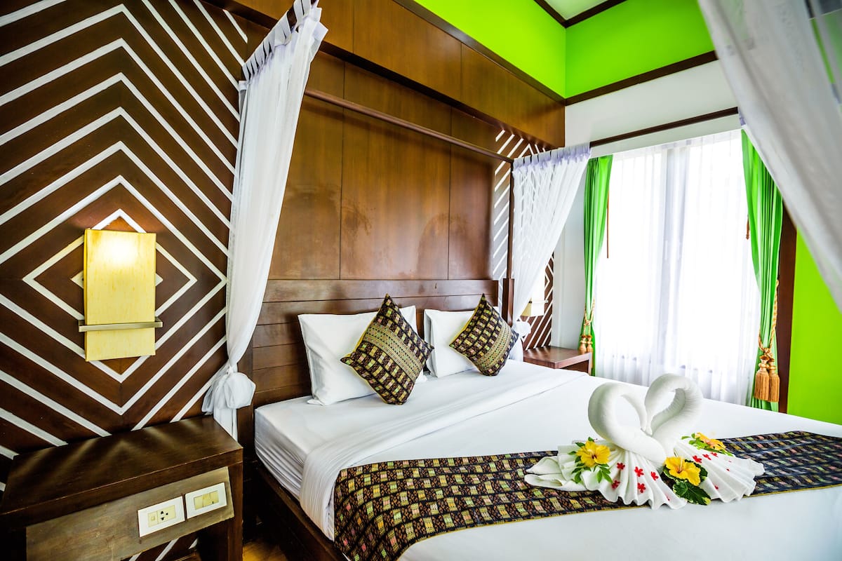 Une chambre d’hôtel avec une tête de lit en bois, un lit recouvert de draps blancs, des oreillers à motifs et un décor central en forme de cygne.