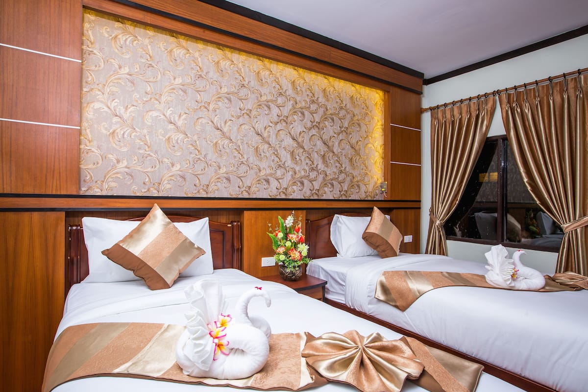 Une chambre d’hôtel avec deux lits, chacun agrémenté d’une serviette pliée en forme de cygne, d’un vase de fleurs et d’un grand panneau décoratif mural.