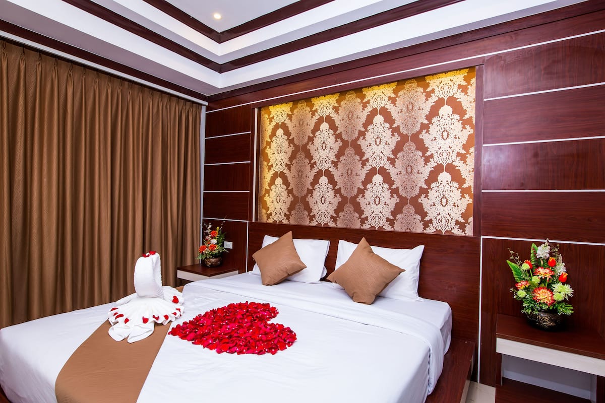 Une chambre d’hôtel avec un grand lit, une tête de lit ornée d’un motif décoratif et une table de chevet agrémentée d’un arrangement floral.
