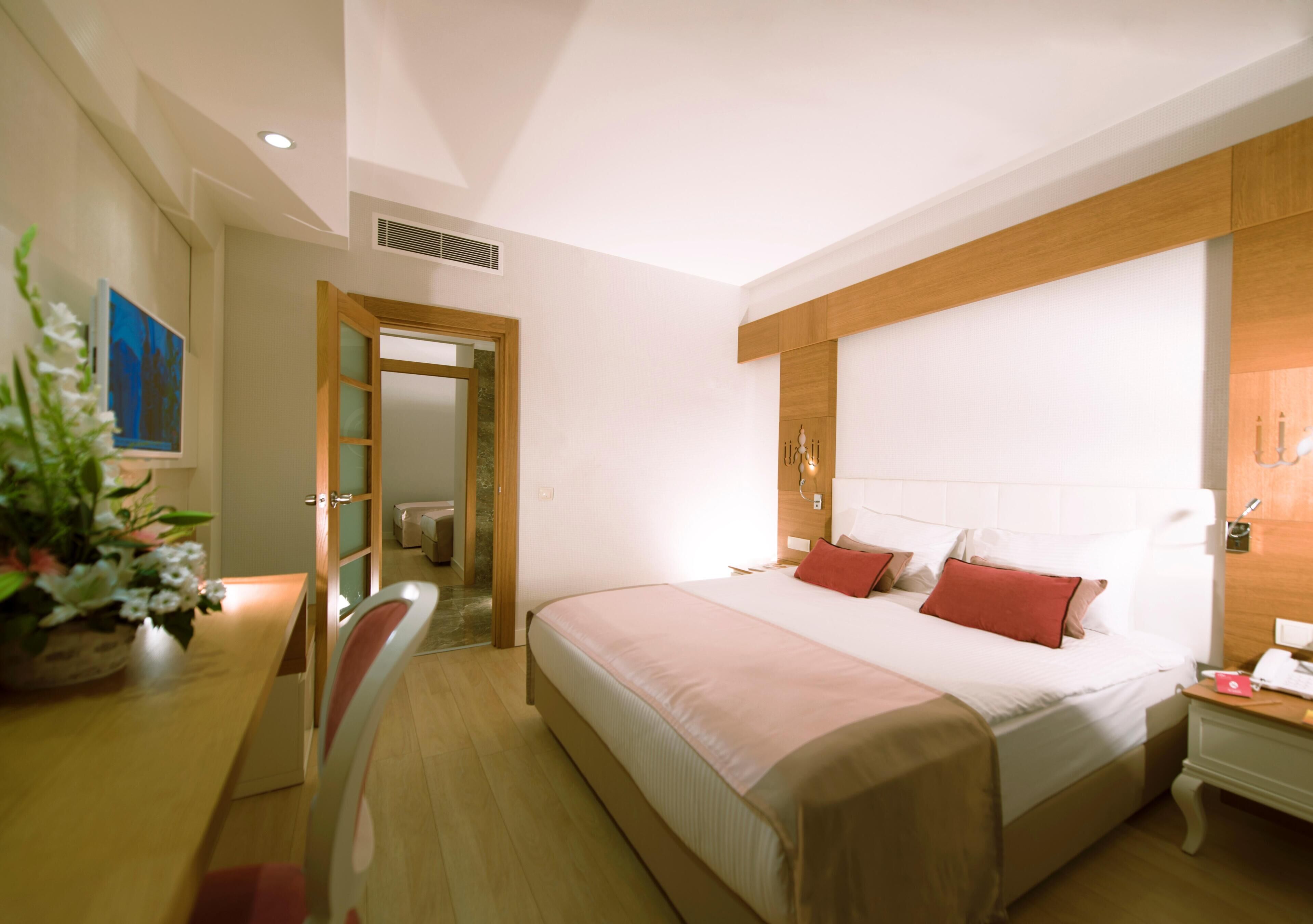 A hotel room with a large bed, bedside table, and a desk with a chair.
