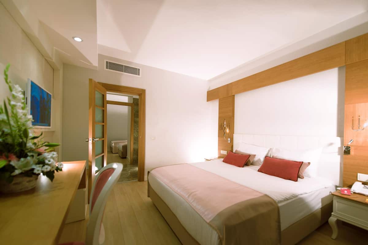A hotel room with a large bed, bedside table, and a desk with a chair.