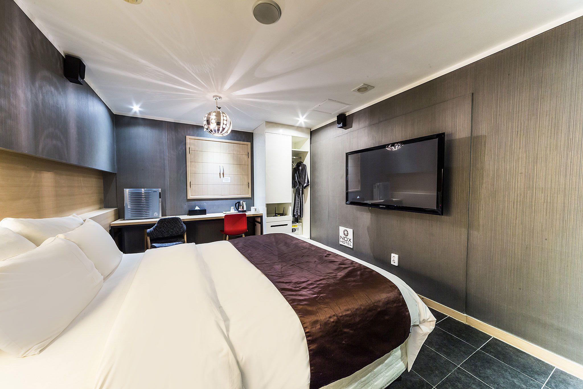A hotel room with a large bed, a desk with a chair, a TV mounted on the wall, and a wardrobe.