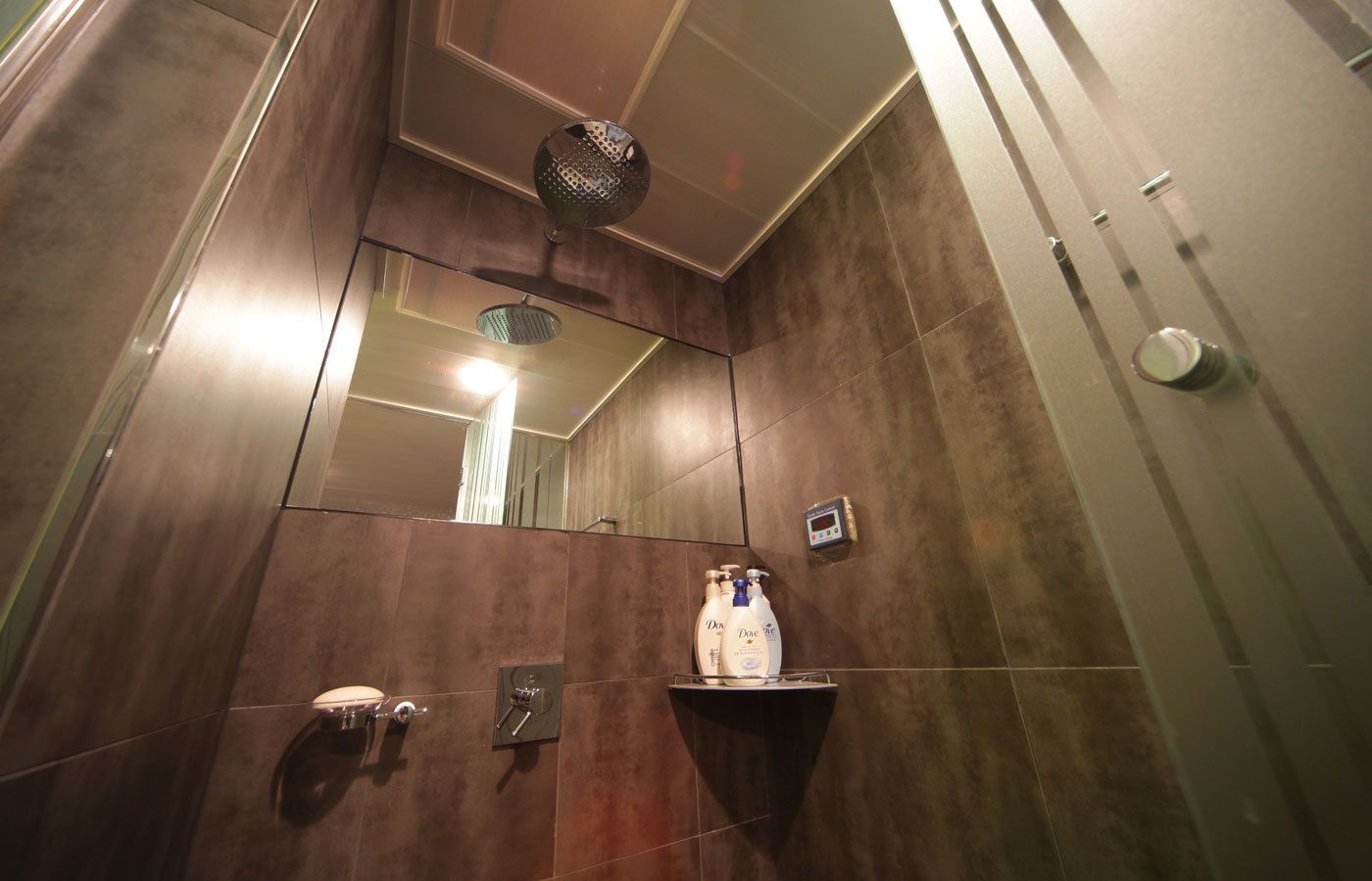 A modern bathroom with a large mirror, a shower head, a towel rack, and a soap dispenser.