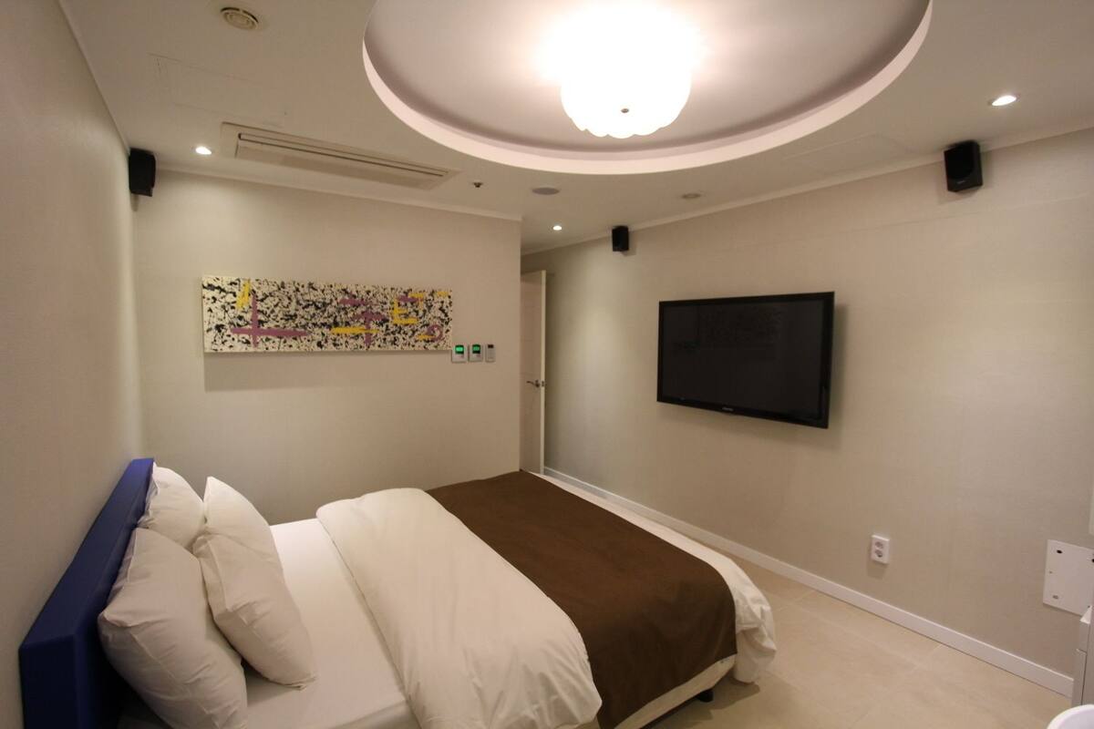A hotel room with a bed, a TV mounted on the wall, and a ceiling light.