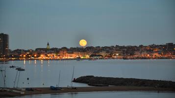 A coastal cityscape at dusk with a prominent full moon, calm water, and buildings with lights.