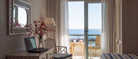 Una camera d'albergo con balcone, una scrivania con un portatile, una sedia, un letto e vista mare.