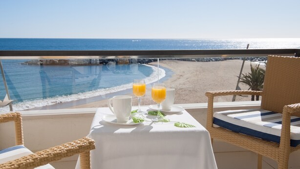 A balcony with a table set for two, overlooking a beach and ocean. - Hotel Rosamar (Calonge)