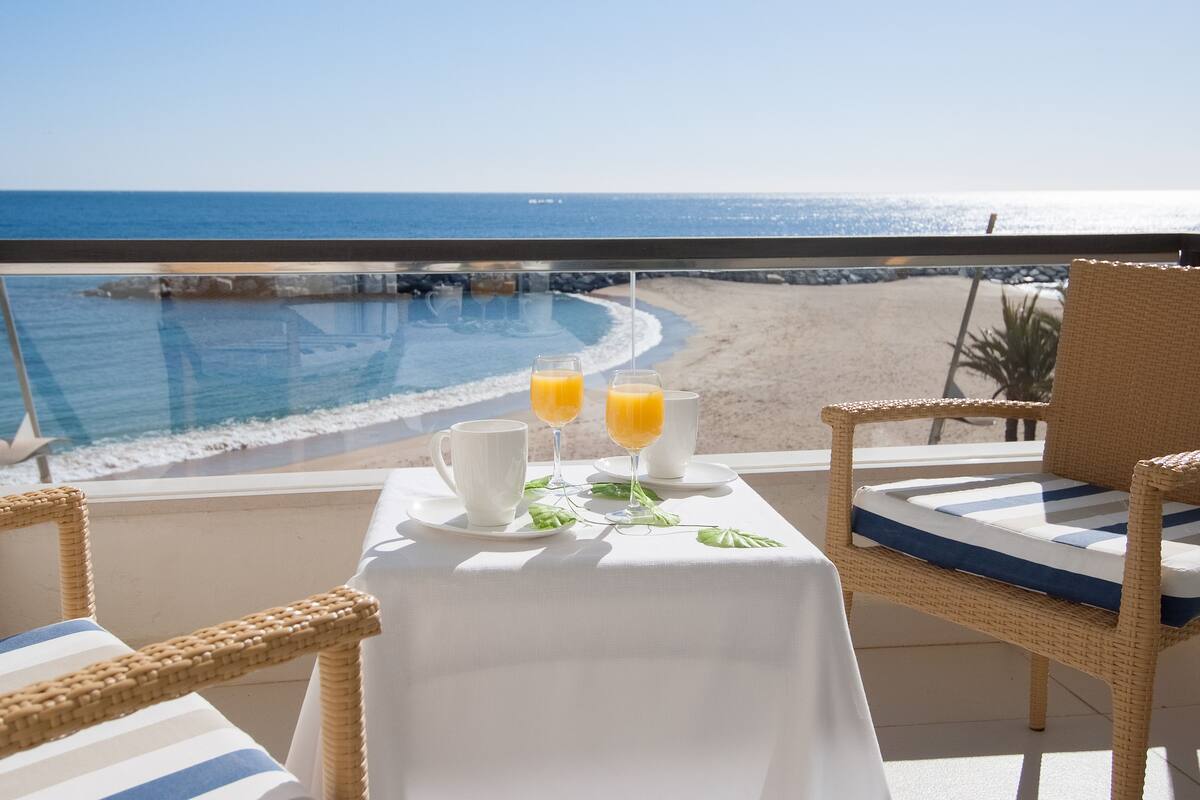 A balcony with a table set for two, overlooking a beach and ocean.