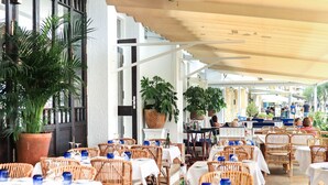 An outdoor dining area with wicker chairs and tables, potted plants, and a wooden pergola. - Hotel Rosamar (Calonge)