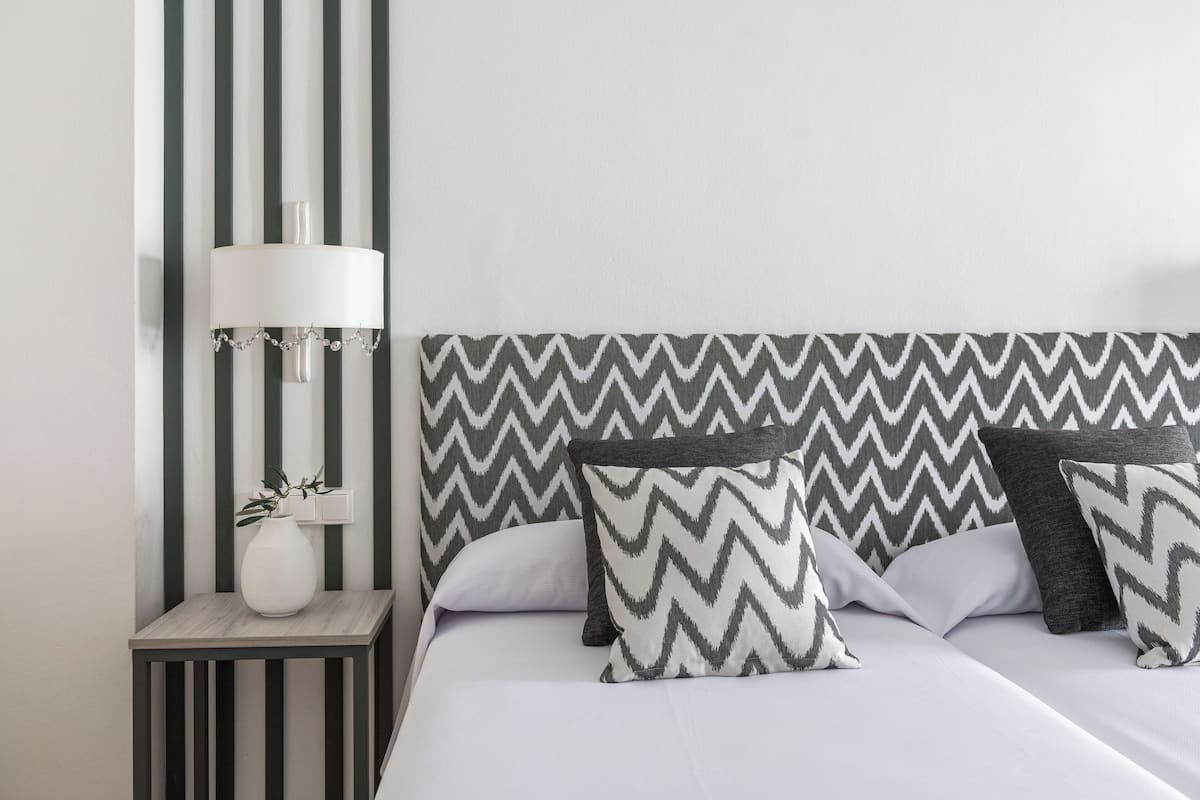A neatly arranged bedroom with a bed, pillows, a bedside table, and a lamp.