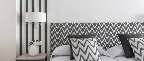 Une chambre à coucher bien rangée, avec un lit, des oreillers, une table de chevet et une lampe.