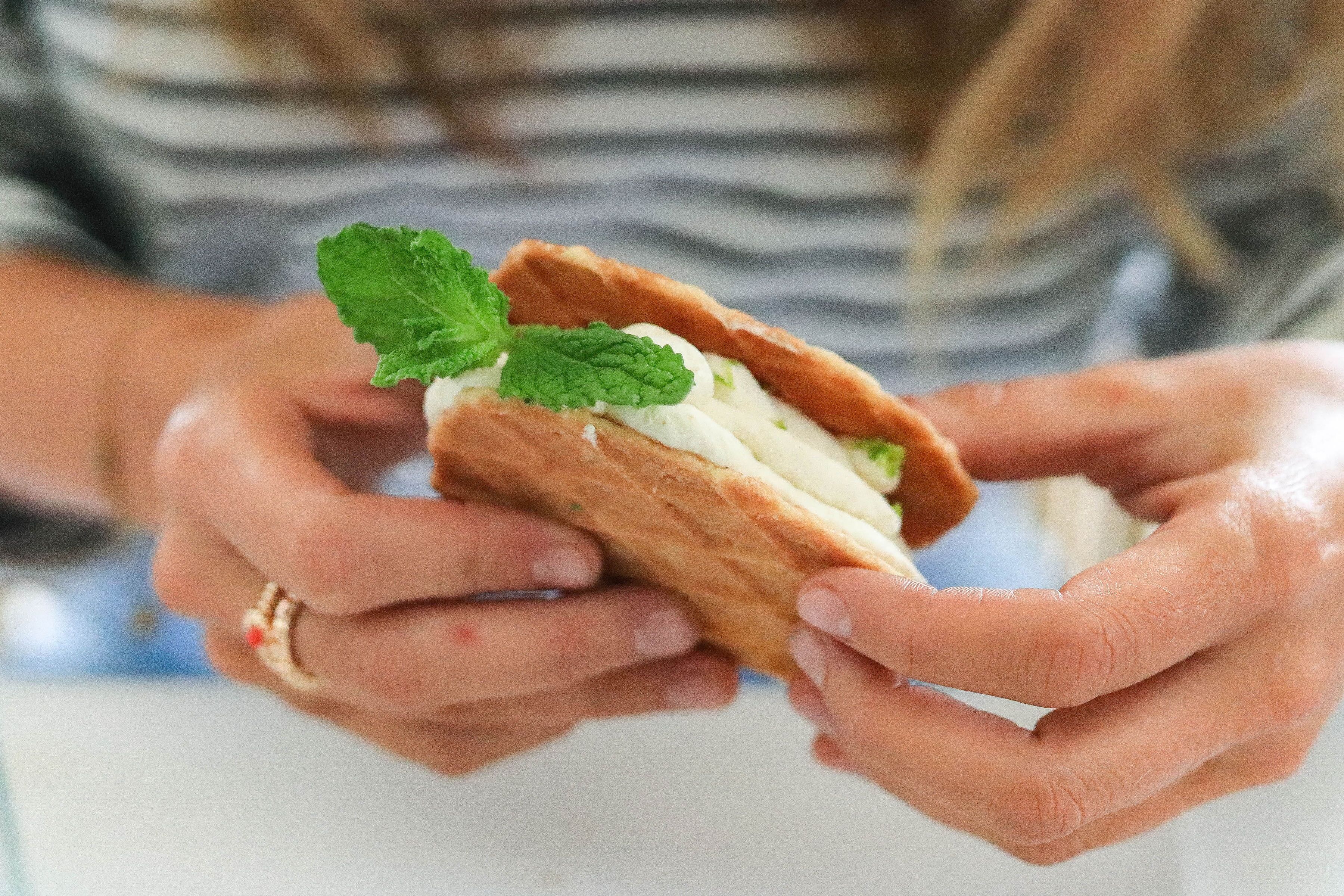A person holding a pastry with a mint leaf garnish.