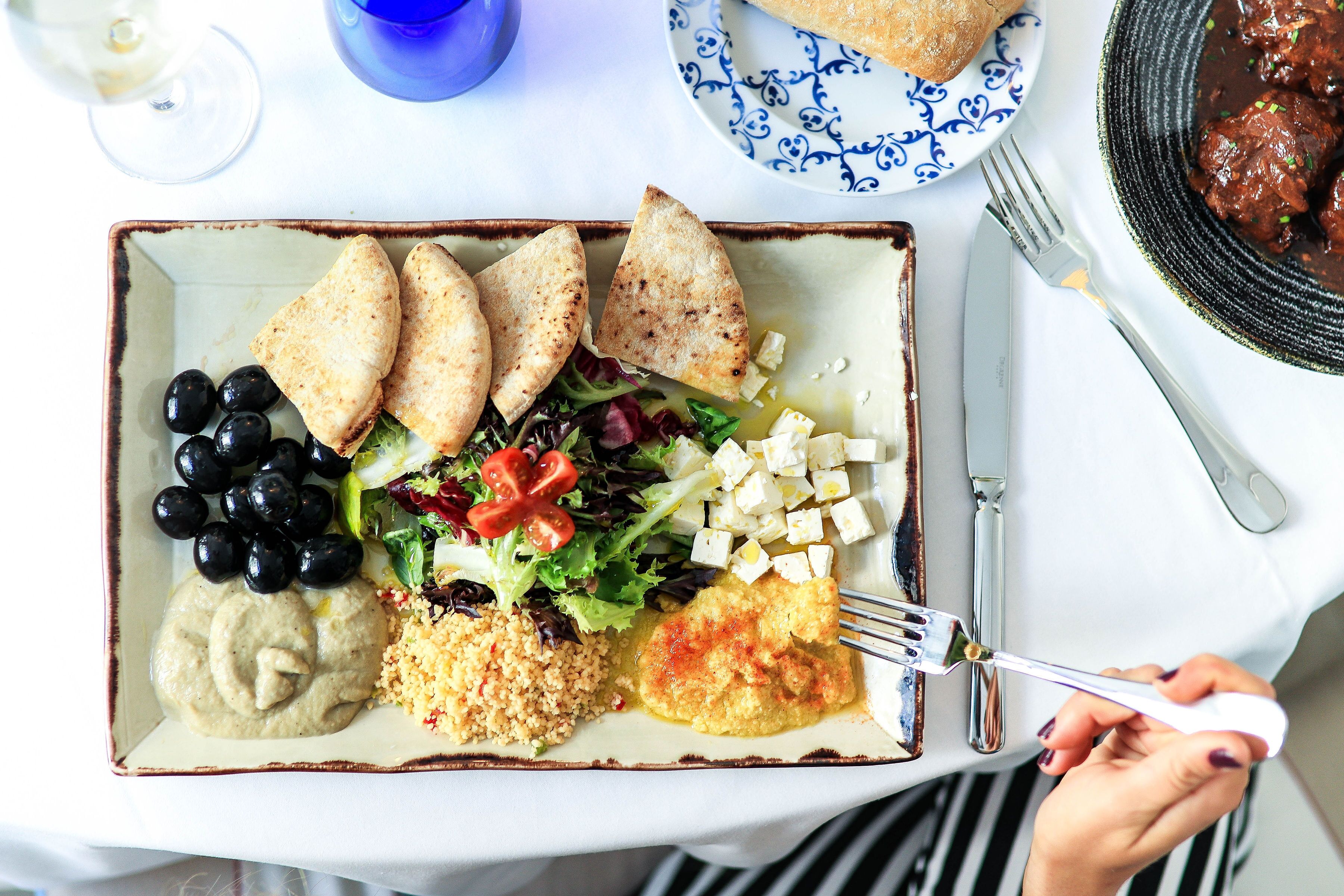 Een maaltijd met diverse gerechten, waaronder brood, olijven, salade en een portie hummus.