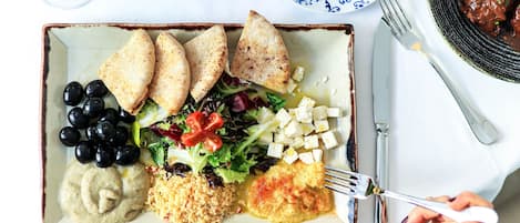 Een maaltijd met diverse gerechten, waaronder brood, olijven, salade en een portie hummus.