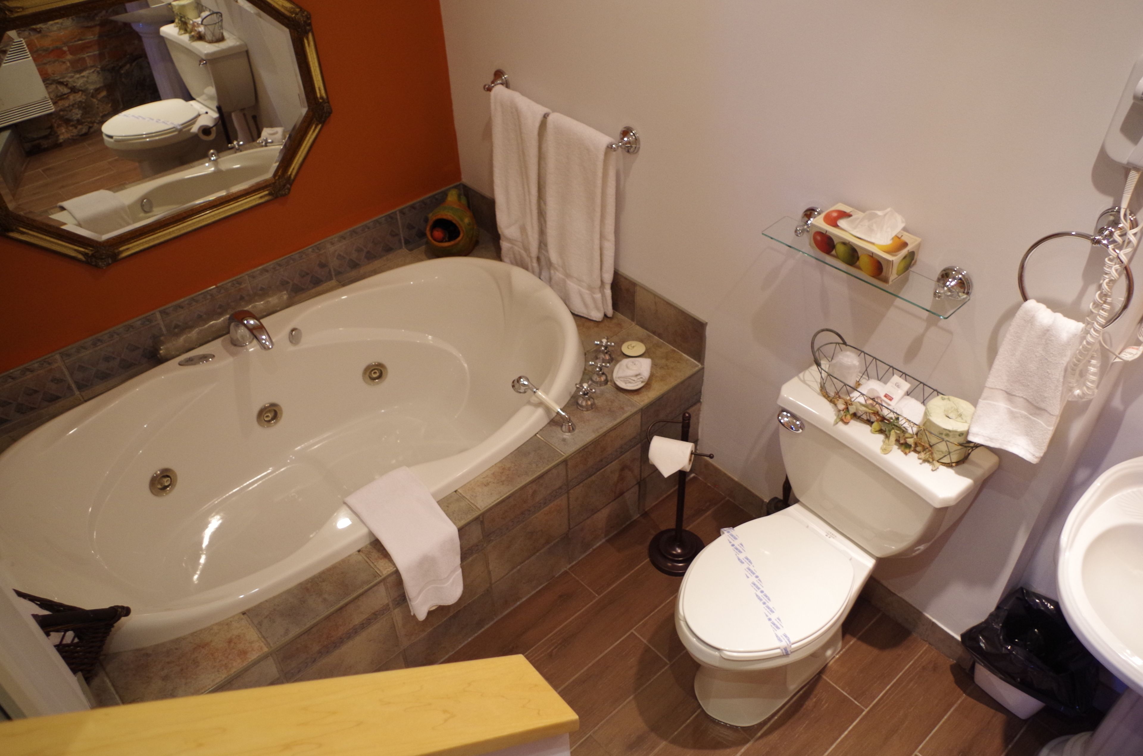 Et badeværelse med badekar, toilet og en glashylde med toiletartikler.