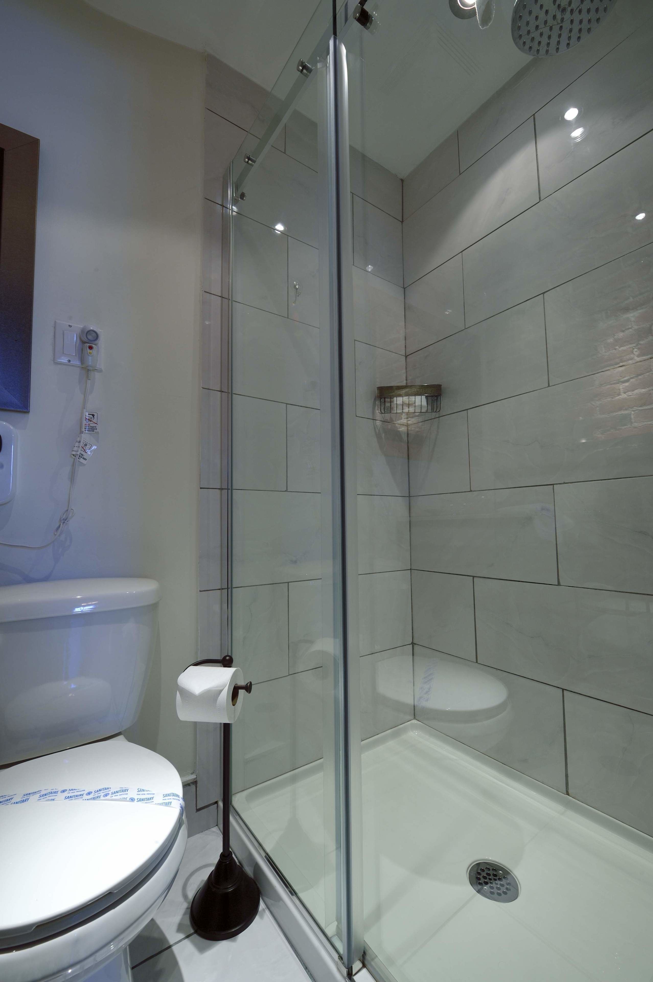A modern bathroom with a glass-enclosed shower, a toilet, and a wall-mounted hand dryer.