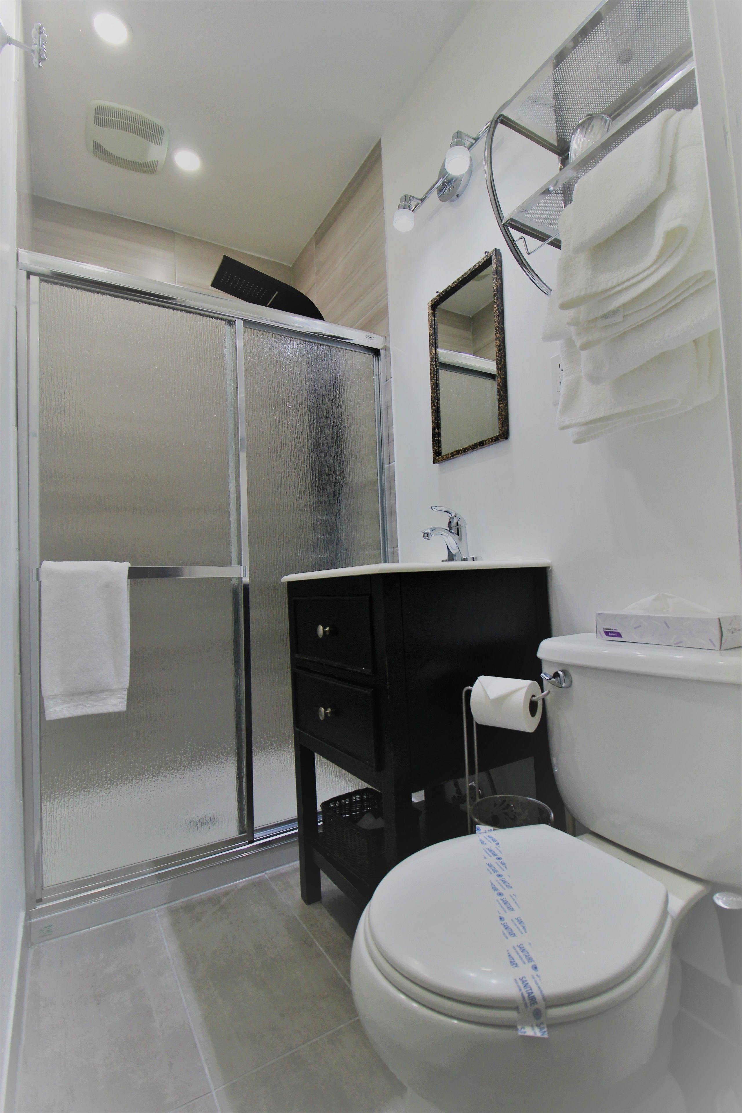 A bathroom with a glass shower enclosure, a white toilet, a black vanity, and a mirror above the sink.