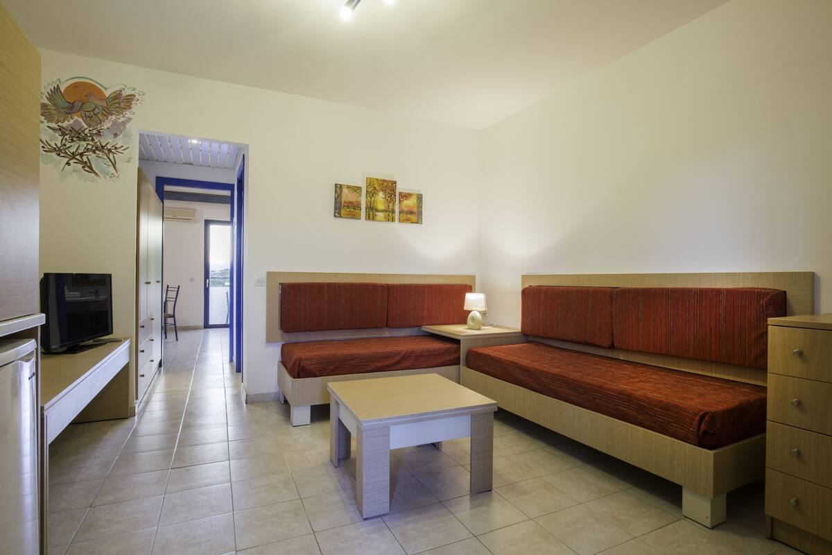 Une chambre d’hôtel moderne et bien éclairée, équipée d’un canapé, d’une petite table, d’une télévision et d’un meuble de rangement.