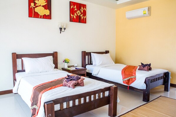 Habitación de hotel con dos camas de madera, ropa de cama blanca, una mesita de noche con lámpara y un aire acondicionado instalado en la pared.