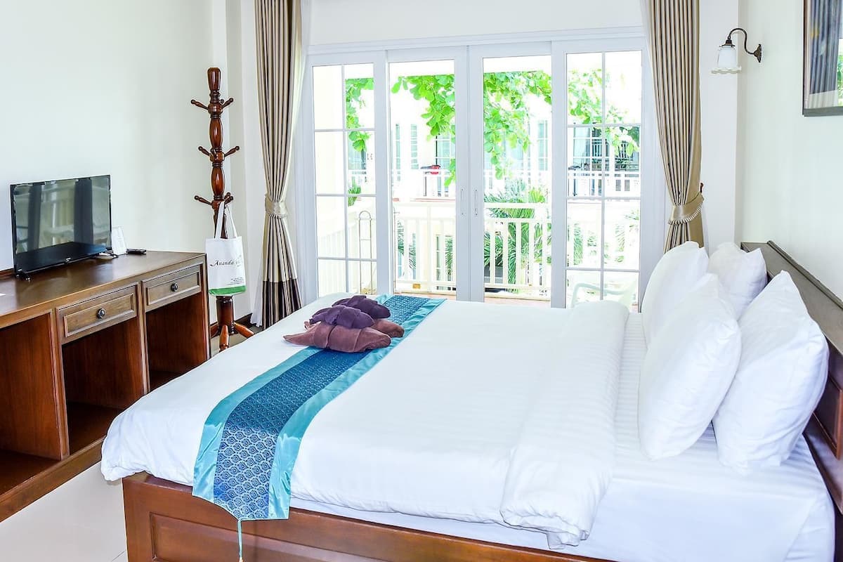 A hotel room with a large bed, a desk with a television, and a view of greenery outside.